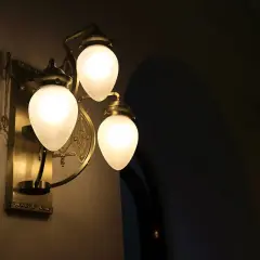 Elegancka, mosiężna lampa ścienna z trzema mlecznymi kloszami. To właśnie takie lampy dają najwięcej światła, tworząc ciepłą atmosferę.