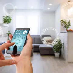 Dłoń steruje aplikacją "Smart Home" na telefonie, symbolizującą inteligentne życie i komfortowe mieszkanie.
