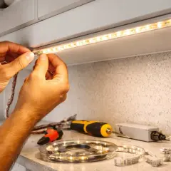 Ręce montują taśmę LED pod szafką. Obok leżą narzędzia i akcesoria do mi light programowania.