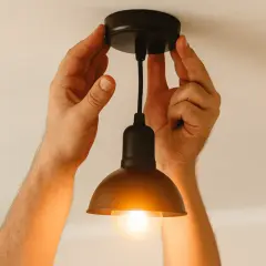 Dwie ręce montują lampę sufitową. Włączone migające światło w domu tworzy ciepłą atmosferę.