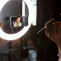 Idealne światło do makijażu: ring light oświetla twarz kobiety nagrywającej tutorial na telefonie.