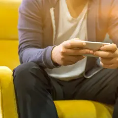 Mężczyzna siedzi na żółtym fotelu, grając na telefonie. Nawet poza siecią, jego **tuya smart** urządzenia działają bez zarzutu.