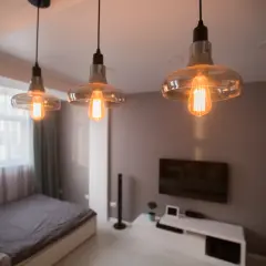 Trzy lampy z żarówkami Edisona tworzą ciepłe światło, idealne, by oświetlić pomieszczenie bez prądu. Wnętrze z łóżkiem i telewizorem.