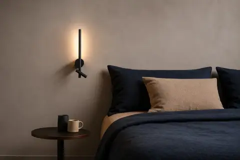 Nowoczesna lampa ścienna z regulowanym kloszem, emitująca światło o kącie świecenia 36 stopni, oświetla przytulną sypialnię z granatową pościelą.