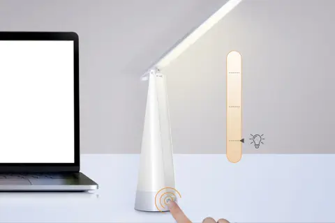 Biała lampka biurkowa z regulacją jasności, obok laptopa. Idealna do czytania, ile lumenów potrzebujesz?