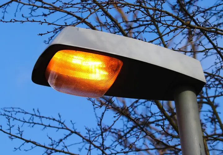 Pomarańczowa lampa uliczna świeci jasno, mimo że jest dzień. Awaria oświetlenia ulicznego?