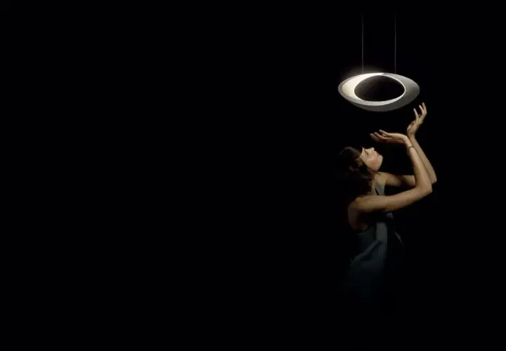 Kobieta wyciąga ręce do nowoczesnej lampy wiszącej, która wygląda jak pierścień. Skracanie lampy wiszącej pozwala na stworzenie intymnej atmosfery.