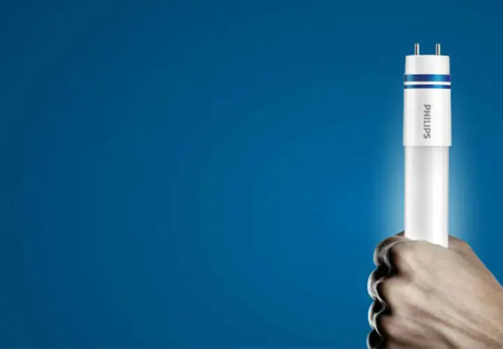 Dłoń trzyma nową żarówkę LED Philips, gotową do wymiany w tubie oświetleniowej.
