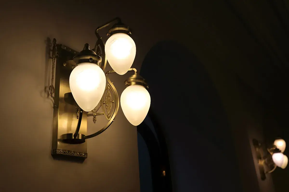 Elegancka, mosiężna lampa ścienna z trzema mlecznymi kloszami. To właśnie takie lampy dają najwięcej światła, tworząc ciepłą atmosferę.