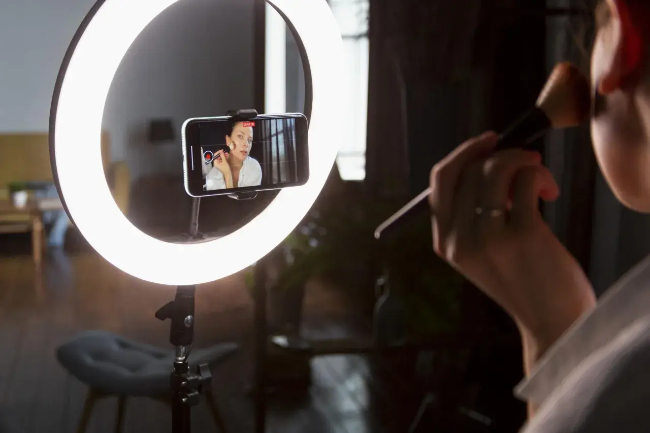Idealne światło do makijażu: ring light oświetla twarz kobiety nagrywającej tutorial na telefonie.