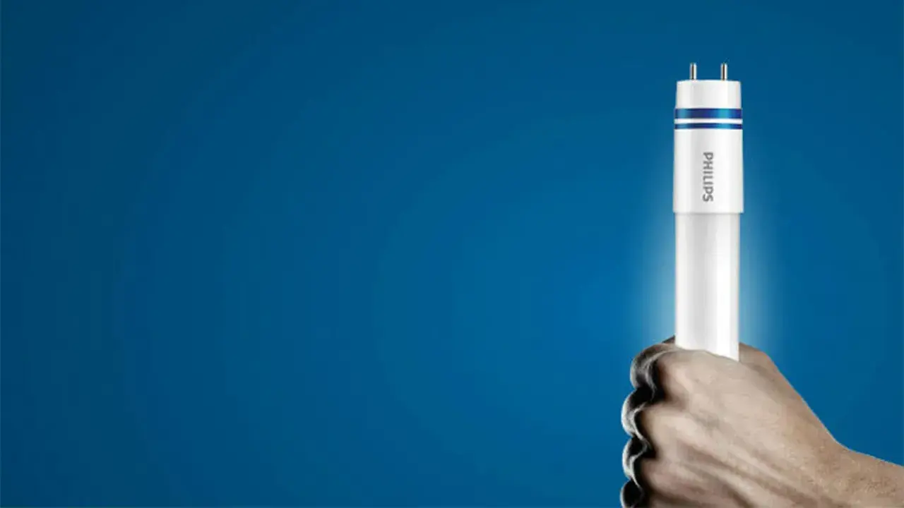 Dłoń trzyma nową żarówkę LED Philips, gotową do wymiany w tubie oświetleniowej.