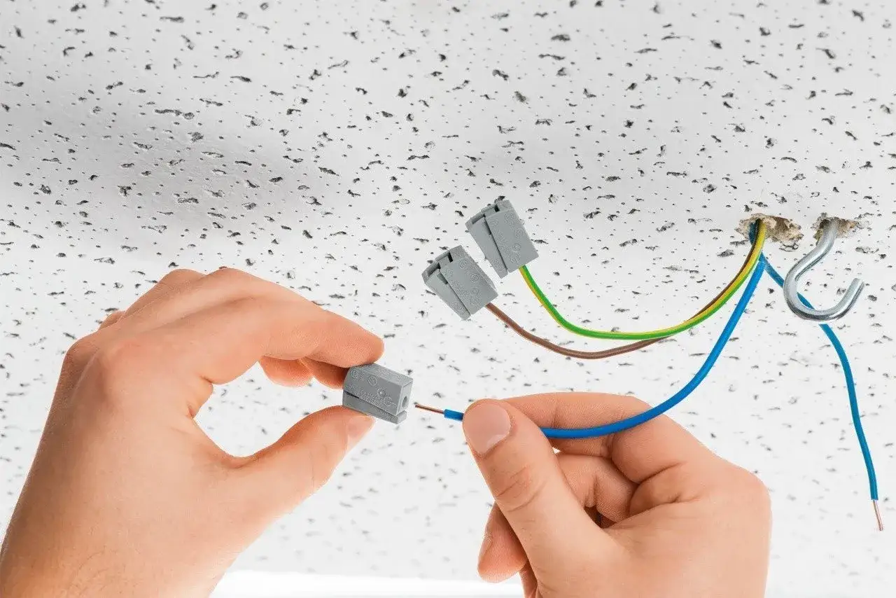 Instalacja elektryczna: jak pociągnąć prąd z lampy. Ręce łączą przewody za pomocą złączek do sufitu podwieszanego.